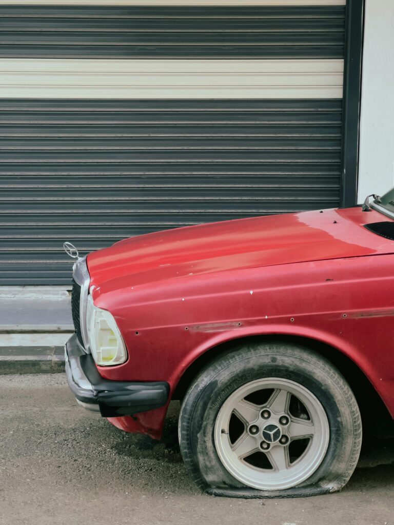 A classic red car with a deflated tire parked in front of a garage door.